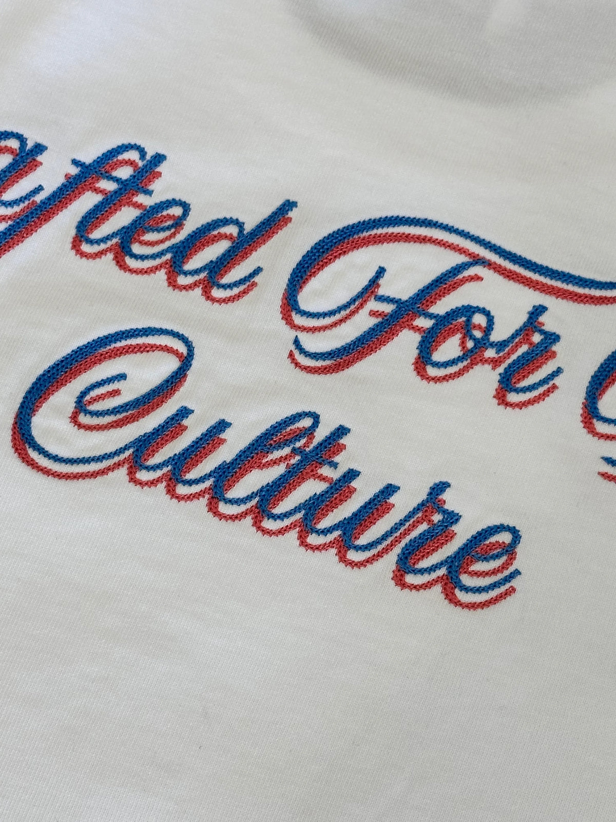 Close-up of blue and red embroidered 'Crafted For Culture' text on white fabric.